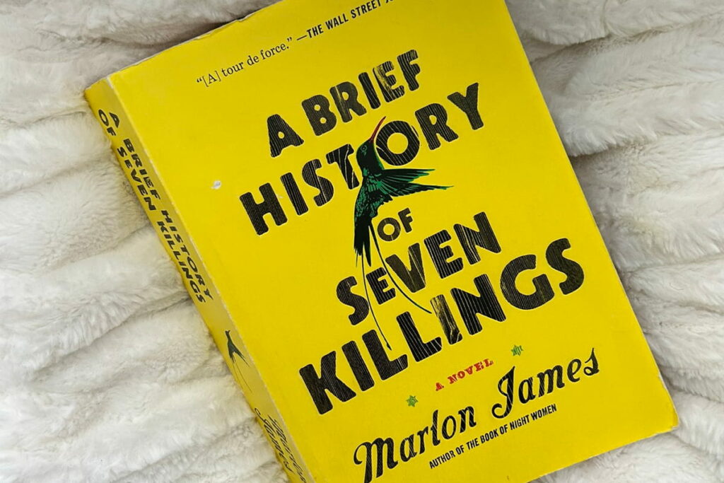 Marlon James' A Brief History of Seven Killings resting on a bed, perfect for cozy reading during rainy day.