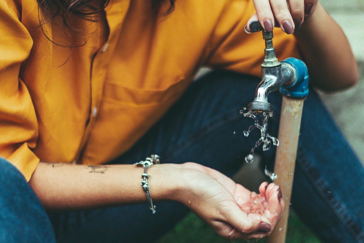 A photo of a woman turning on a tap, with water flowing out of it suggesting that the water in Jamaica is safe to drink.