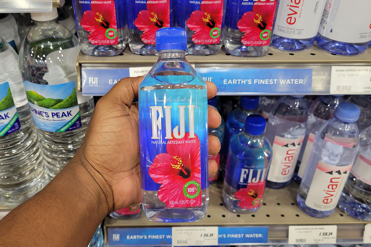 A person holding a bottle of Fiji water in a supermarket in Jamaica.