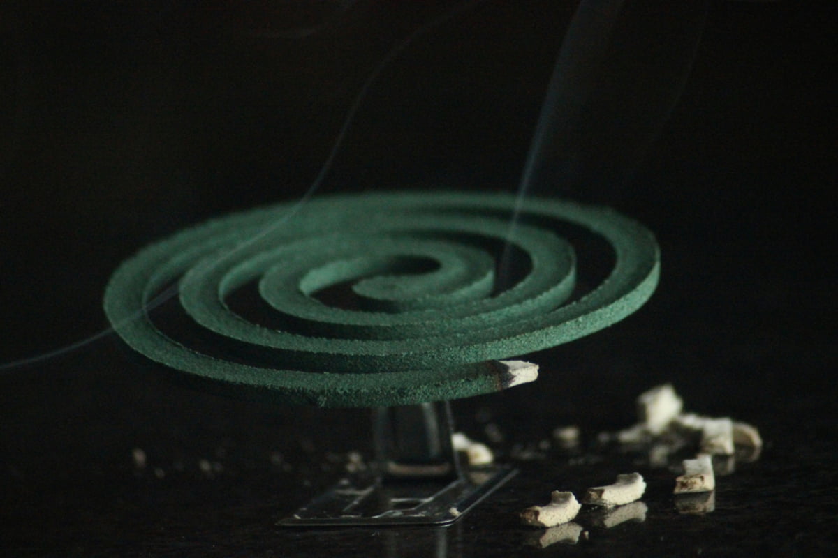 Mosquito destroyer coil burning on a metal stand with smoke rising.