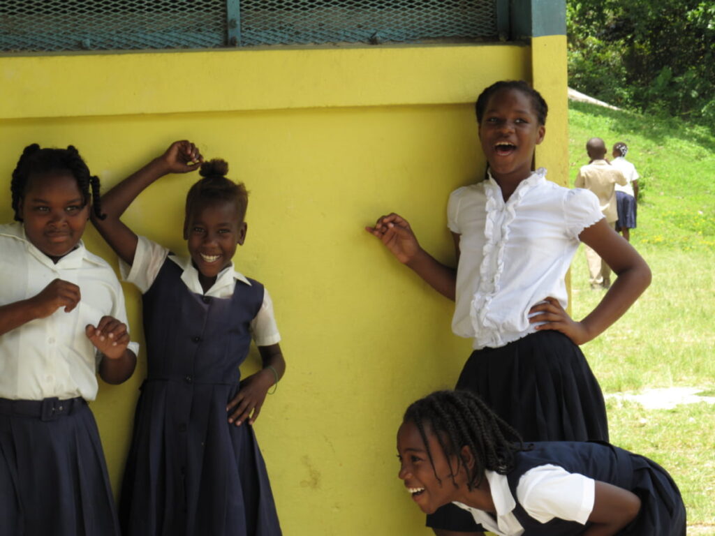 happy Jamaican schoolgirls in their school uniforms, laughing at the camera