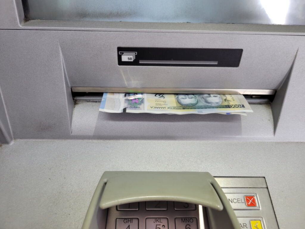 An ATM in Jamaica dispensing several new Jamaican dollar banknotes, showing a common way for travelers to get local currency.