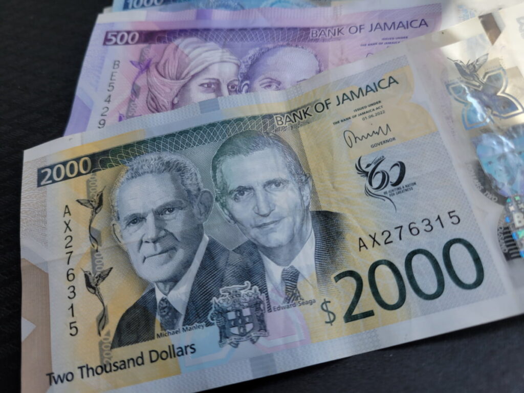 A closeup of several new polymer Jamaican dollar banknotes, showcasing their vibrant colors and detailed designs, representing the currency travelers will get in Jamaica.