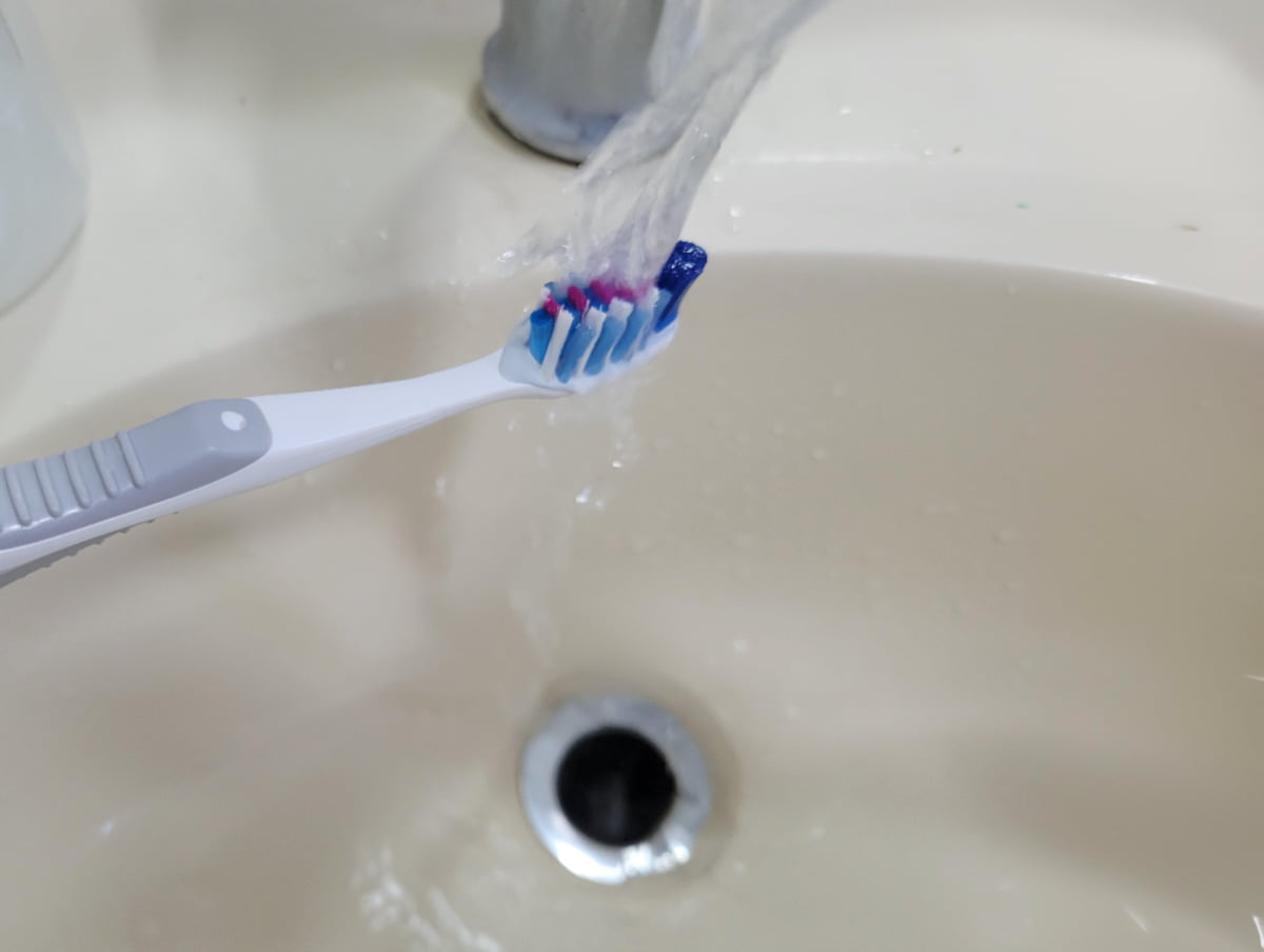 Rinsing a toothbrush under clean, treated tap water from a Jamaican sink.